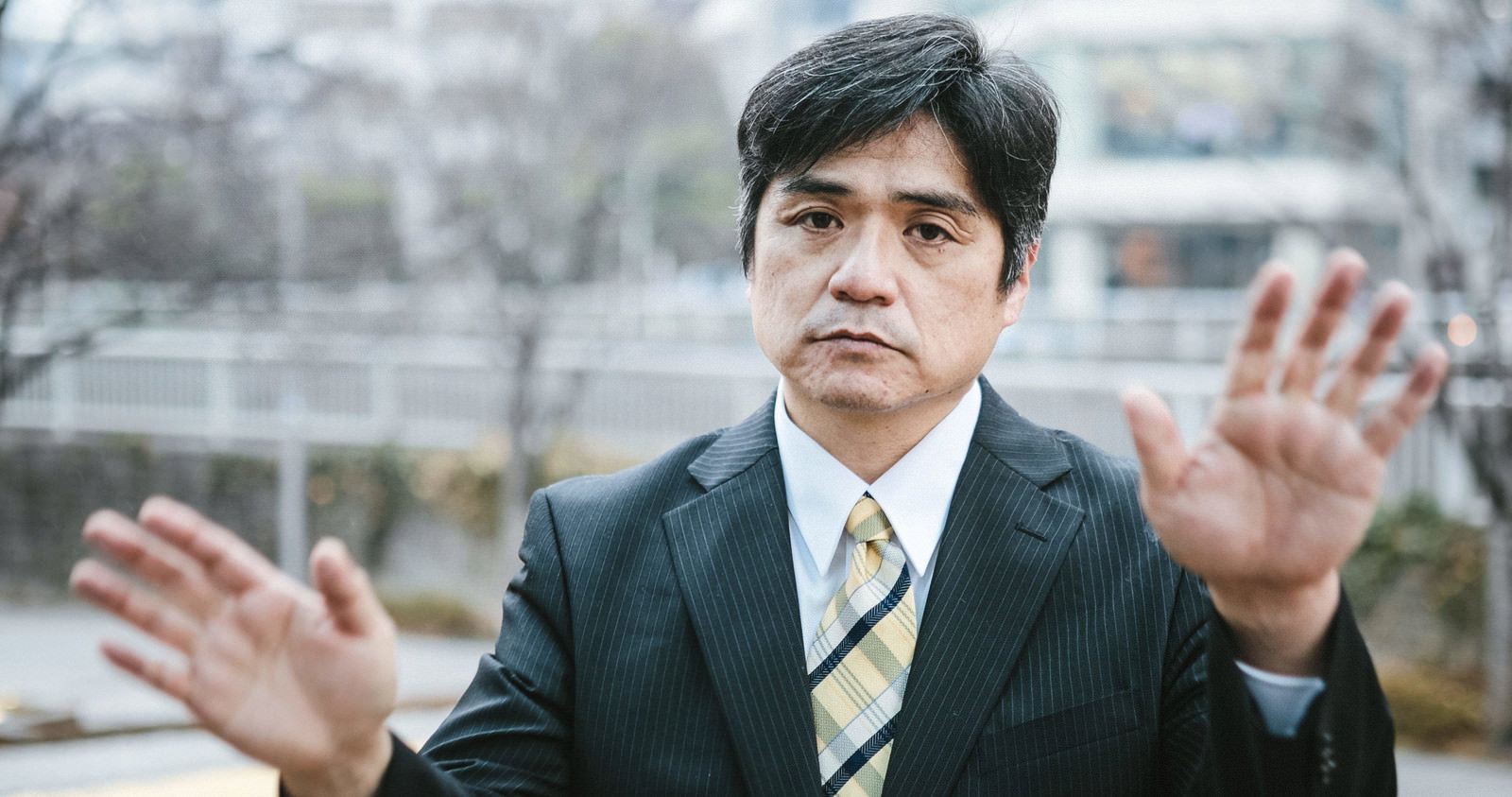 両手を前に出して制止のポーズをとるスーツ姿の男性［モデル：よたか］