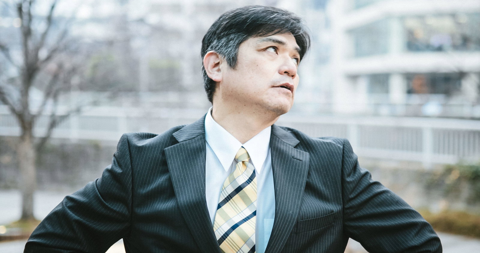 紺色のスーツを着た男性が屋外で空を仰ぎ見上げている様子［モデル：よたか］