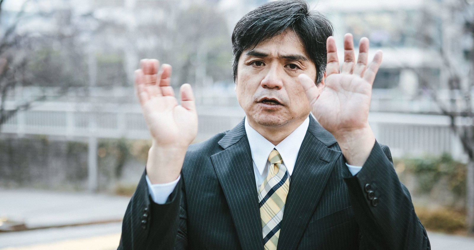 両手を挙げてお手上げのポーズをとるスーツ姿の中年男性部長［モデル：よたか］