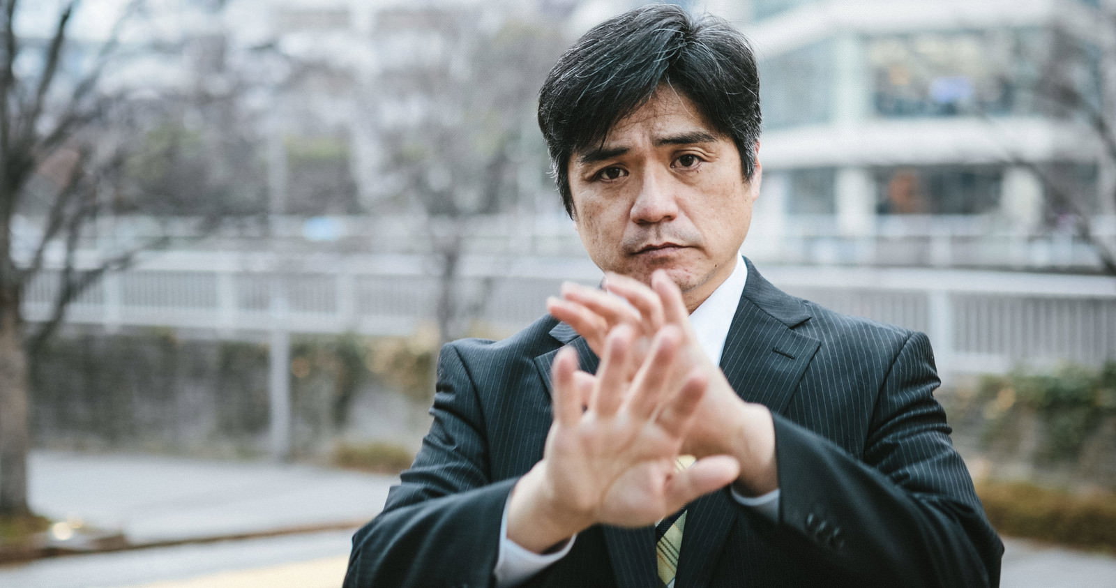 黒いスーツを着た男性が手を前に出してNOサインを表示している［モデル：よたか］