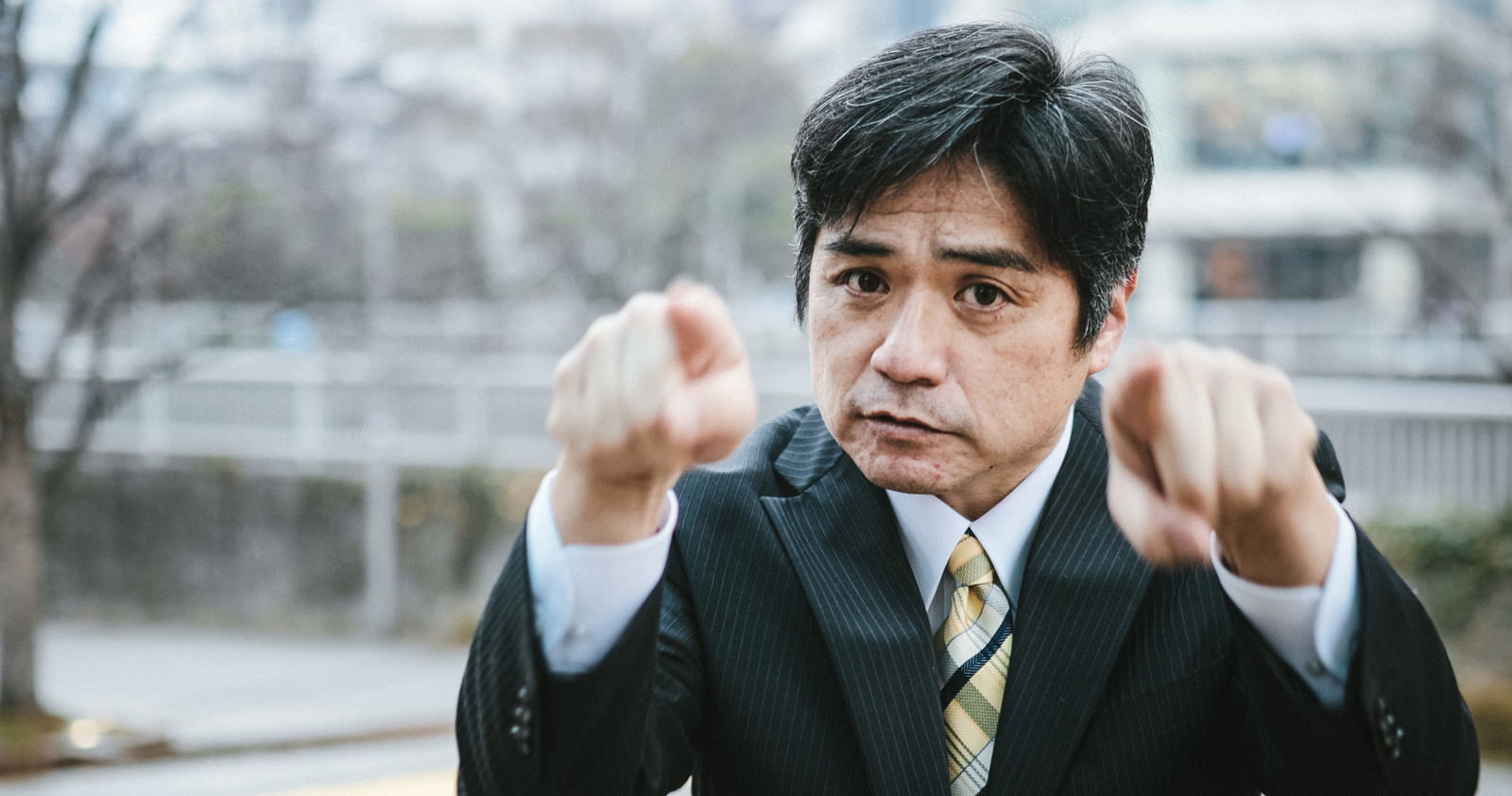 スーツ姿の部長が両手の人差し指を立てて前に突き出している［モデル：よたか］