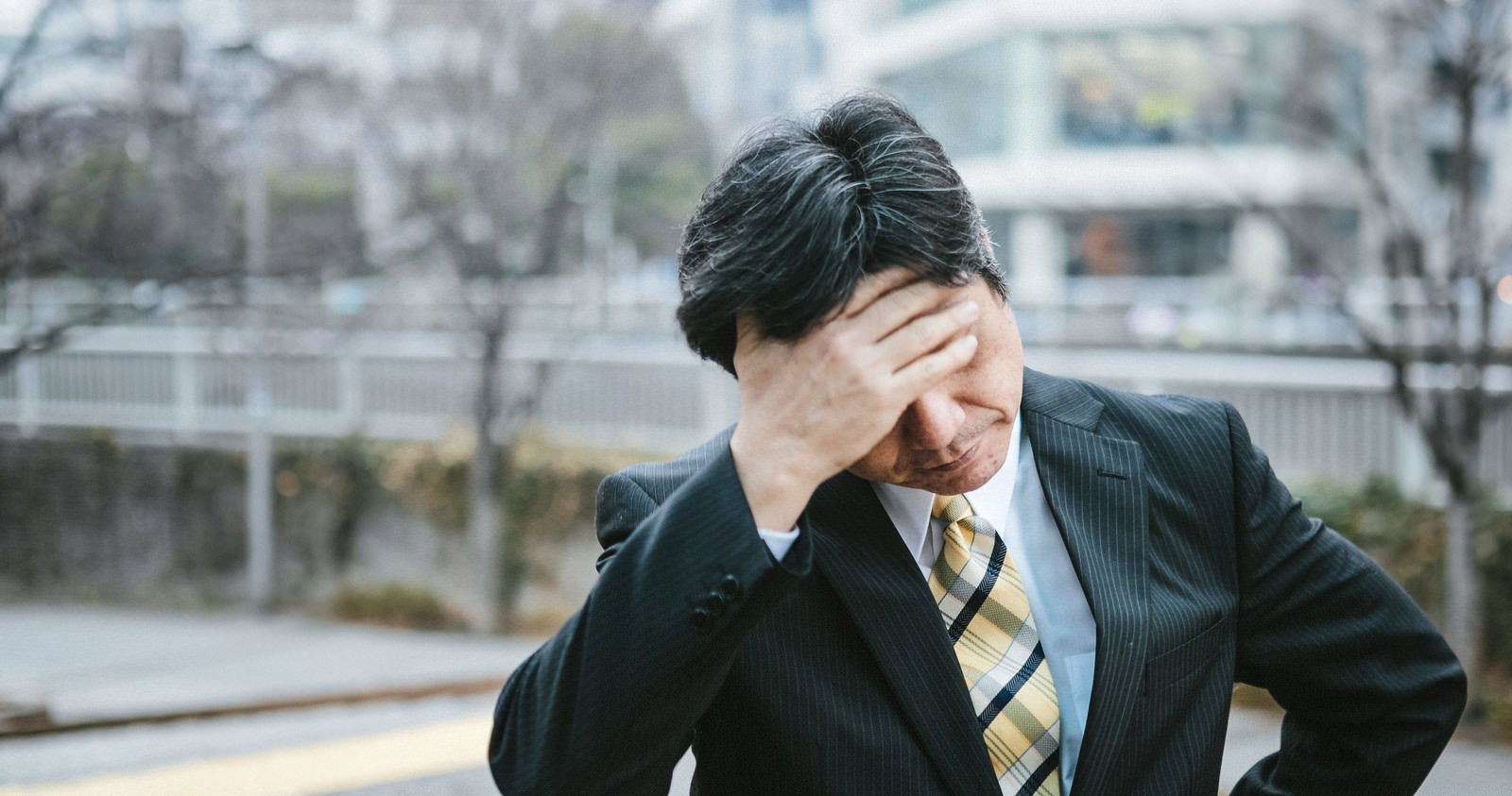 スーツ姿で頭を抱えて悩む中年男性の上司［モデル：よたか］