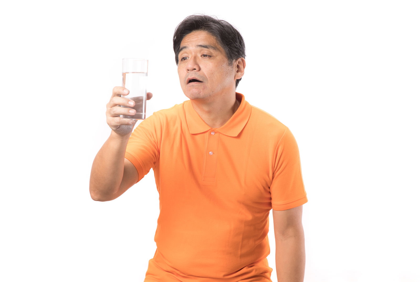 オレンジのシャツを着た中年男性がコップの水を飲んでいる［モデル：よたか］
