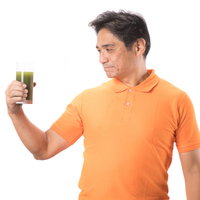 青汁を見つめるオレンジTシャツの中年男性の写真