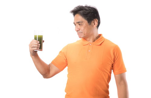 青汁を見つめるオレンジTシャツの中年男性