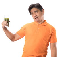 苦い青汁を見て顔がひきつるオレンジTシャツの中年男性の写真