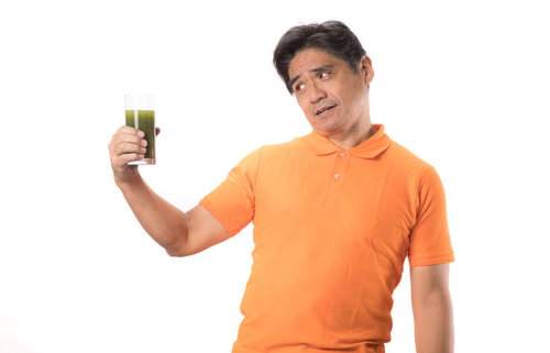 苦い青汁を見て顔がひきつるオレンジTシャツの中年男性