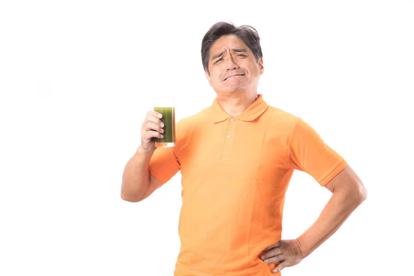 オレンジ色のシャツを着た中年男性が青汁を飲んで苦そうな表情をしている様子［モデル：よたか］