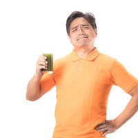 あぁ苦いもういっぱい、オレンジシャツの中年男性が青汁を飲むの写真