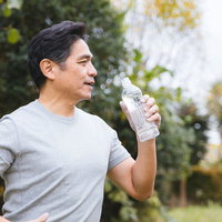 緑の公園でミネラルウォーターを飲む中年男性の水分補給の写真