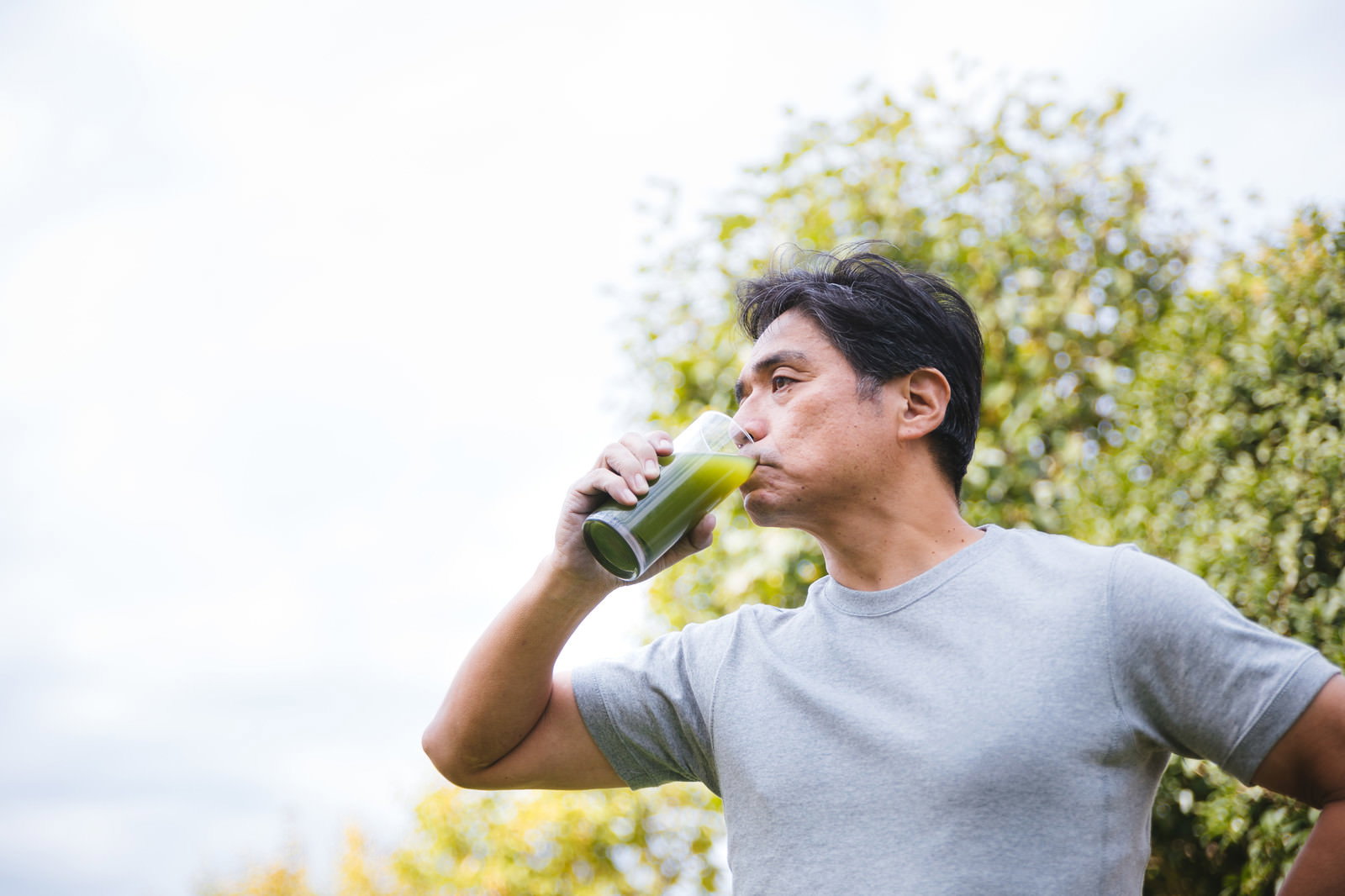 屋外で青汁を飲む中年男性の様子［モデル：よたか］
