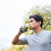 天気がいい日は外で青汁をゴクゴク飲む中年男性の写真