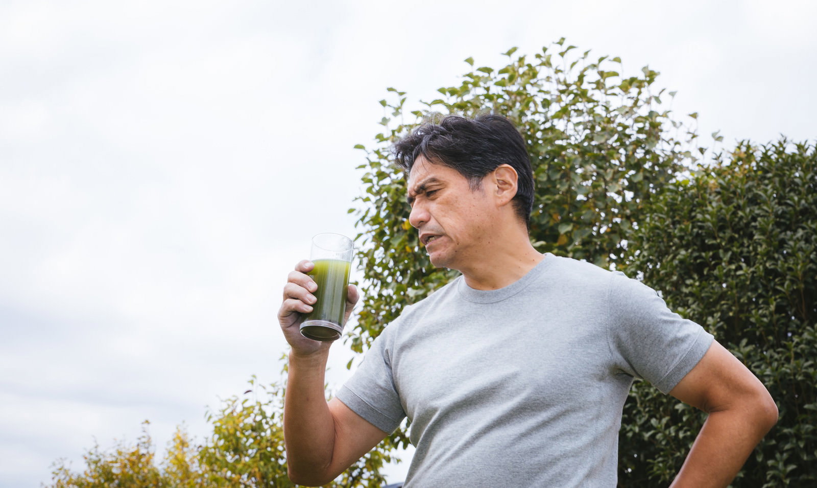 青汁を飲んで苦い表情をする中年男性［モデル：よたか］
