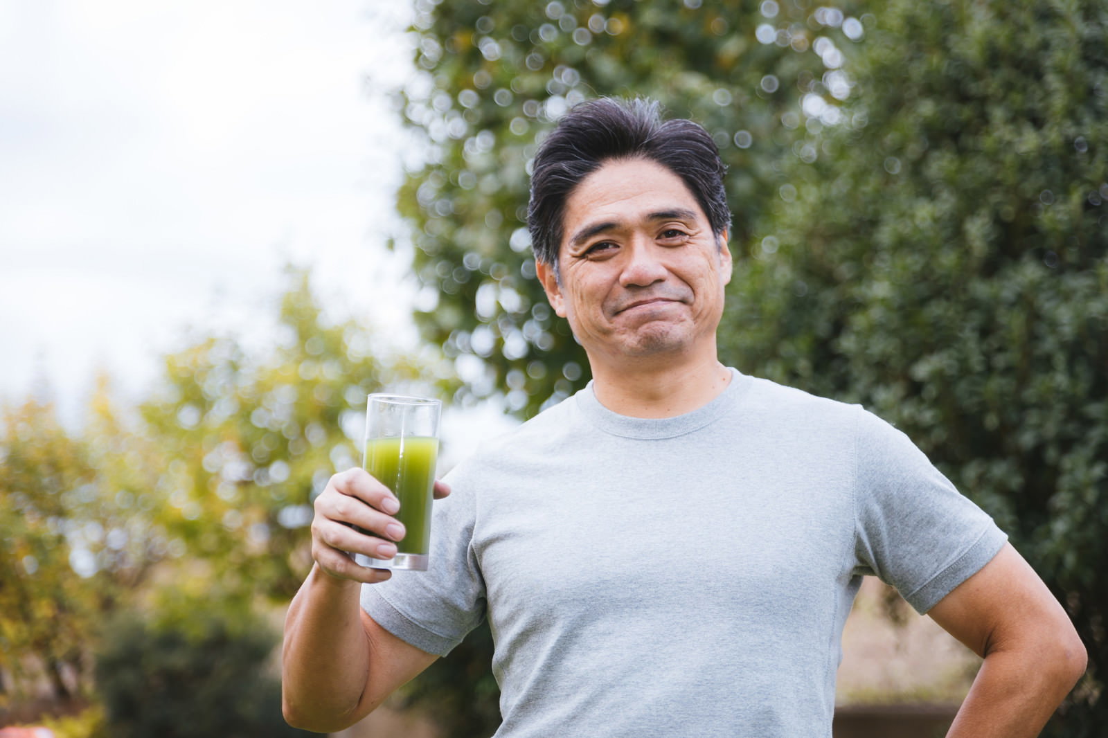 青汁を手に持ちながら爽やかな笑顔を見せる中年男性［モデル：よたか］