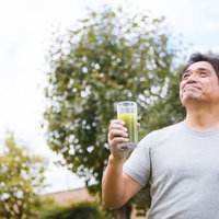 庭でグレーのTシャツを着て青汁を飲むお父さんの写真