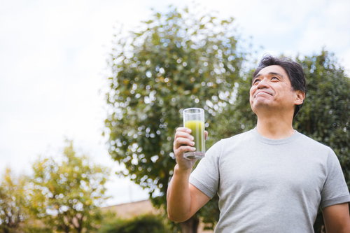 庭でグレーのTシャツを着て青汁を飲むお父さん