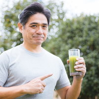 青汁を指差しながら笑顔を見せる健康志向の男性の写真