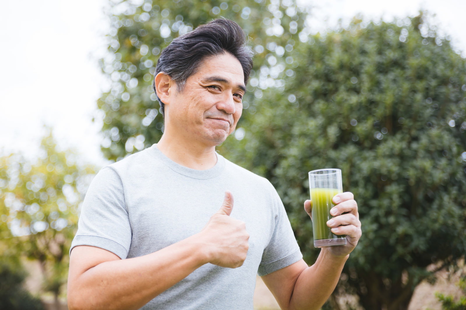 青汁を手に持ち笑顔で親指を立てる中年男性［モデル：よたか］