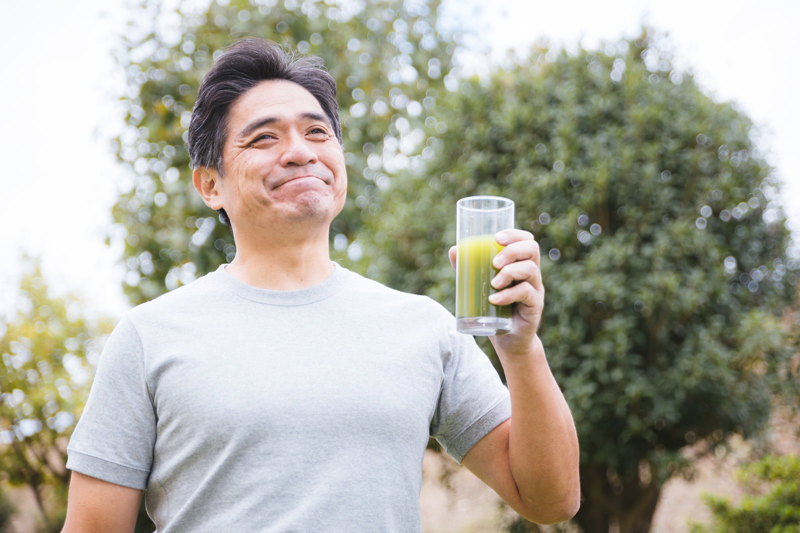 青汁を飲んで満足そうな笑顔を浮かべるグレーTシャツの男性［モデル：よたか］