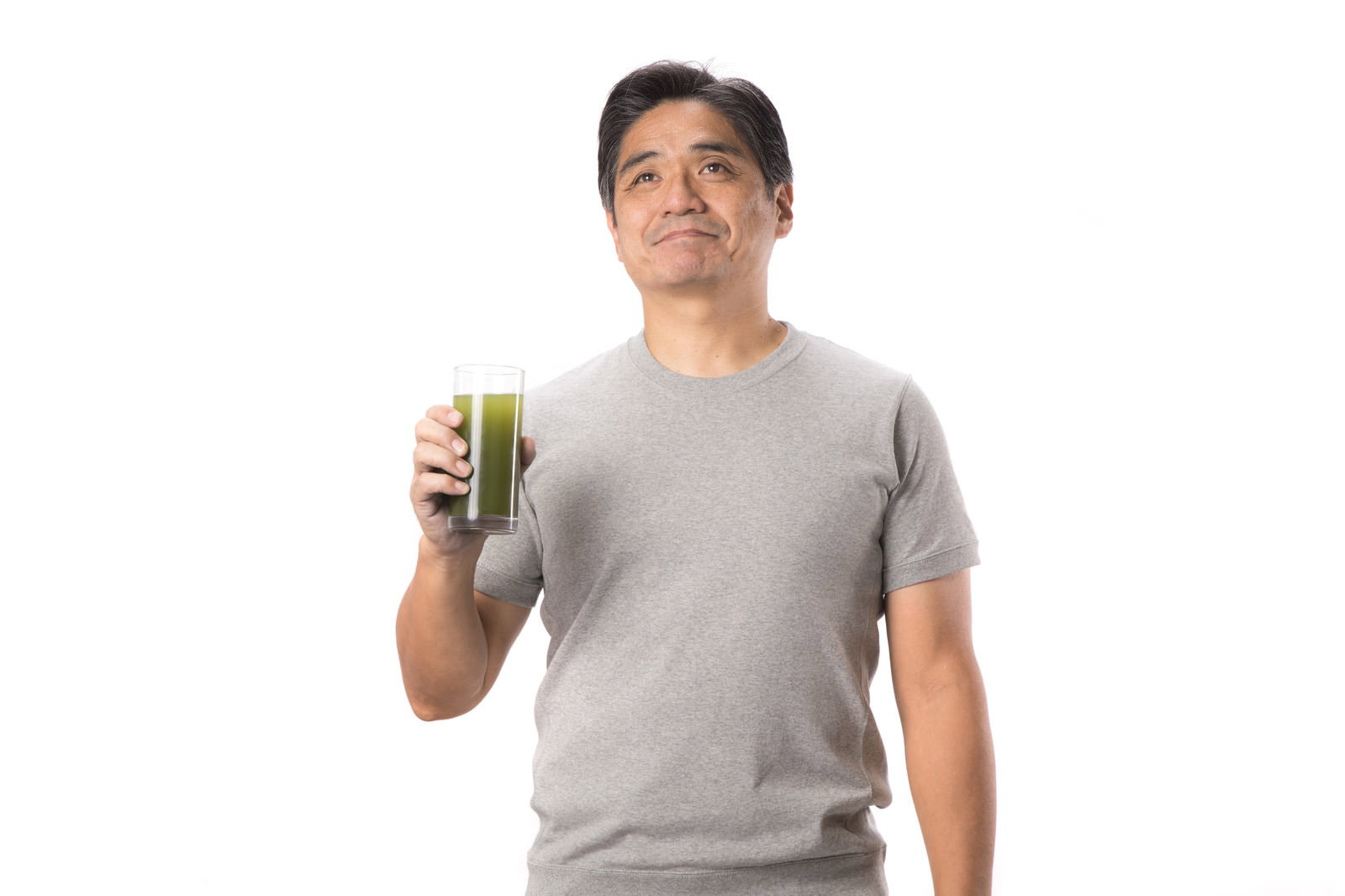 緑色の青汁を手に持ち上を見上げるグレーのTシャツの中年男性［モデル：よたか］