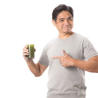 グラスの青汁を親指で指差す中年男性のヘルシーライフスタイルの写真