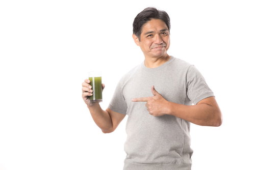 グラスの青汁を親指で指差す中年男性のヘルシーライフスタイル