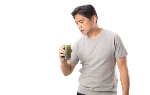 とても苦い青汁を飲んで嫌な顔をする中年男性
