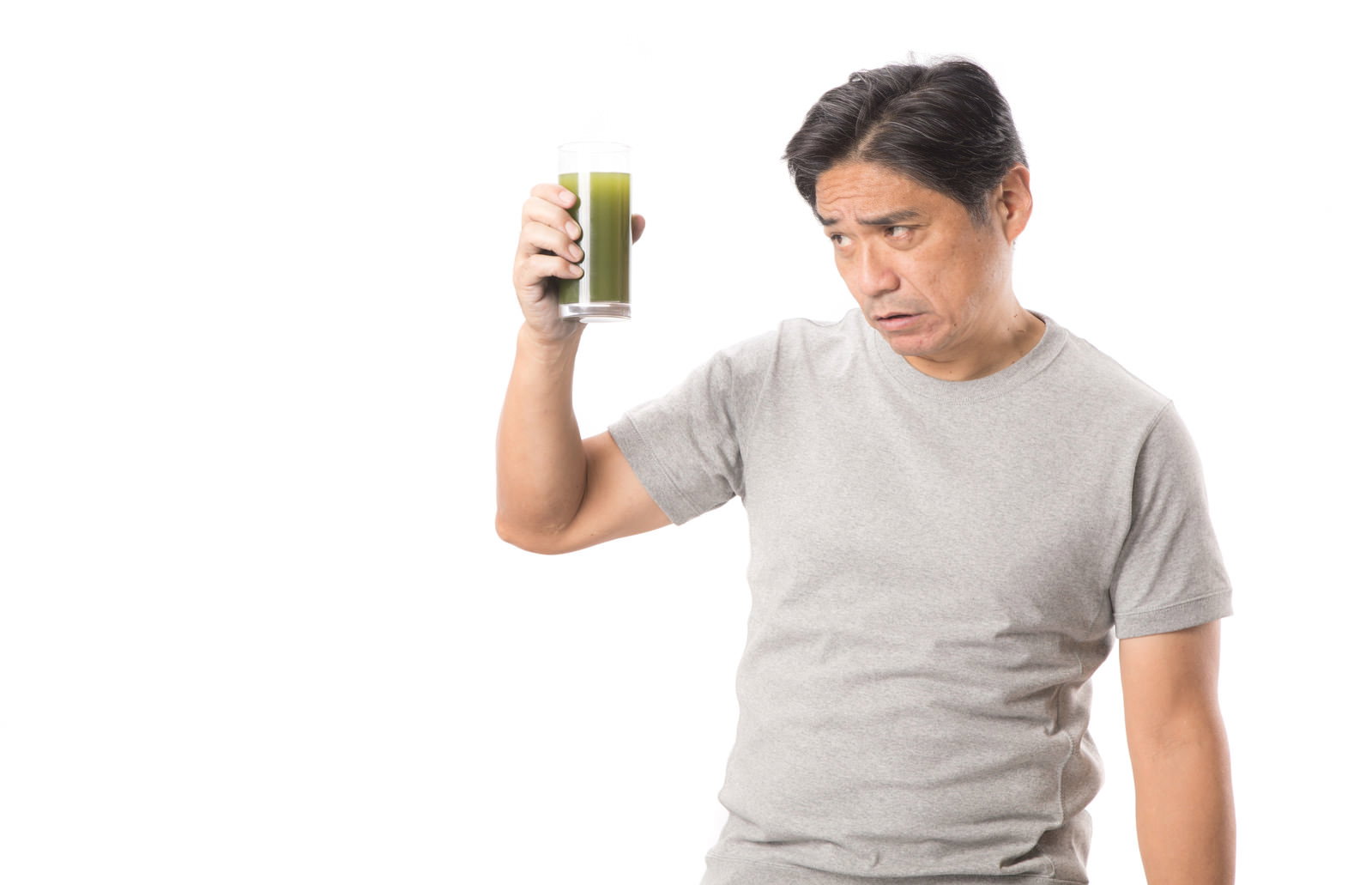 グレーのTシャツを着た中年男性が青汁のグラスを手に持っている［モデル：よたか］