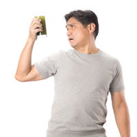 搾りたての青汁を不安な顔で見つめるグレーのTシャツを着た父親の写真