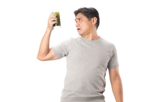搾りたての青汁を不安な顔で見つめるグレーのTシャツを着た父親