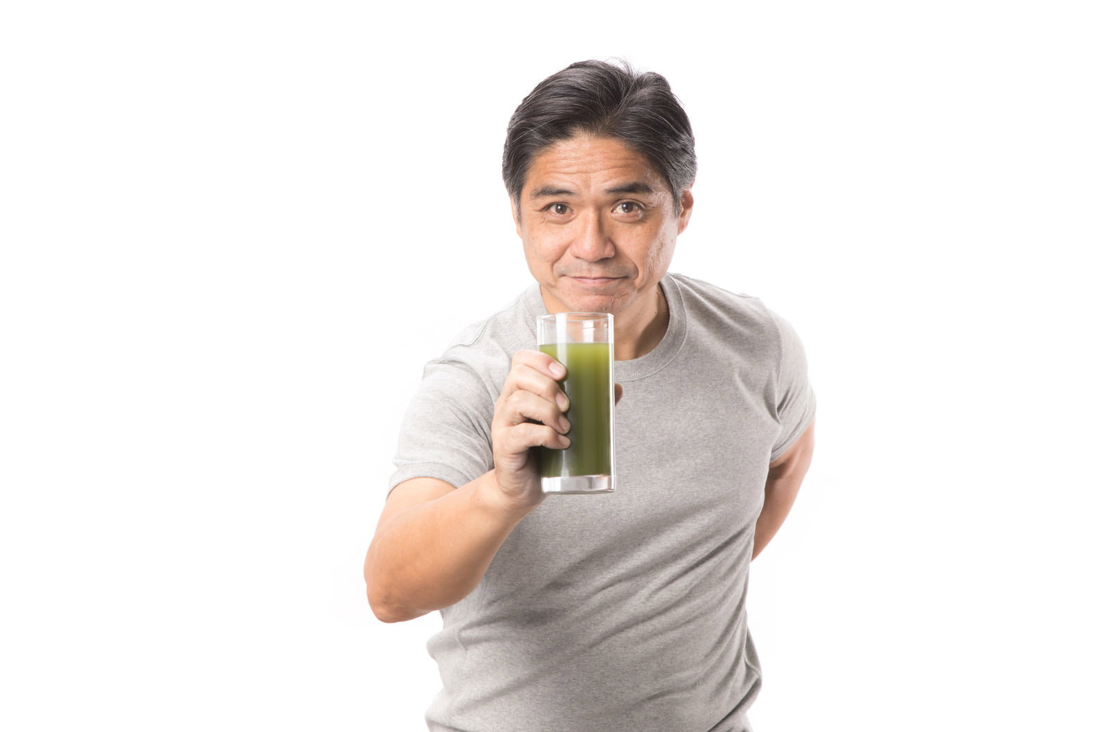 グレーのTシャツを着た中年男性が青汁を飲んでいる［モデル：よたか］