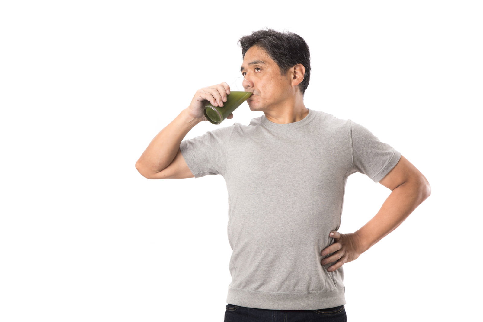 グレーのTシャツを着た中年男性が青汁を飲んでいる様子［モデル：よたか］