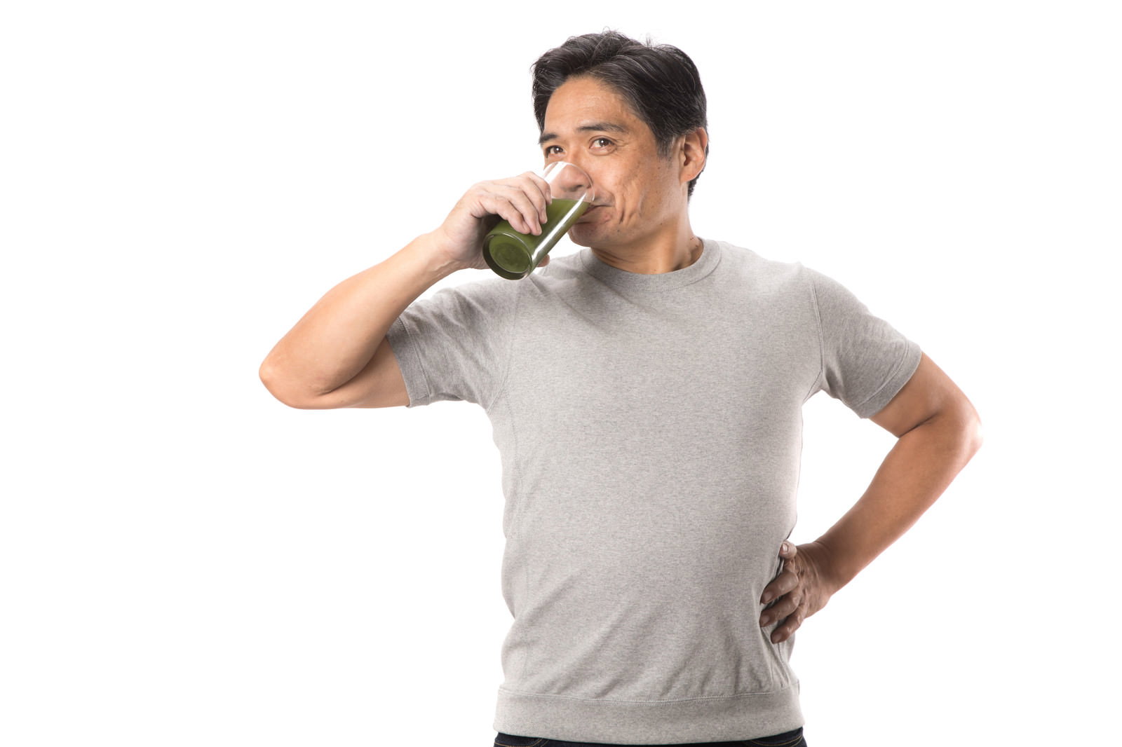 グレーのTシャツを着た中年男性が青汁を飲んでいる様子［モデル：よたか］
