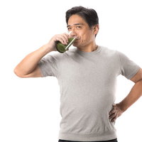 グレーのTシャツを着た中年男性がコップで青汁を飲むの写真