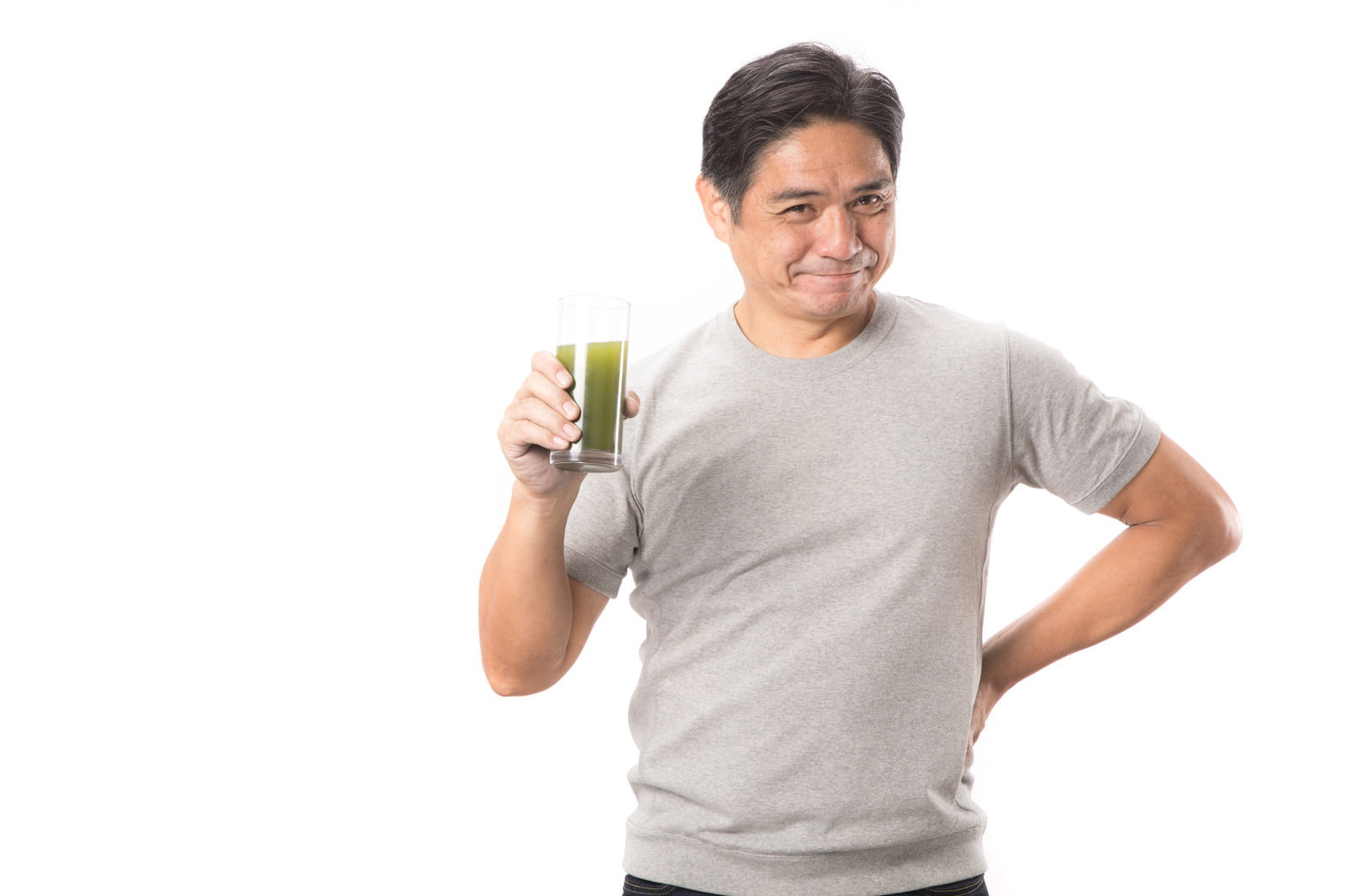 グレーのTシャツを着た中年男性が青汁入りグラスを持つ［モデル：よたか］