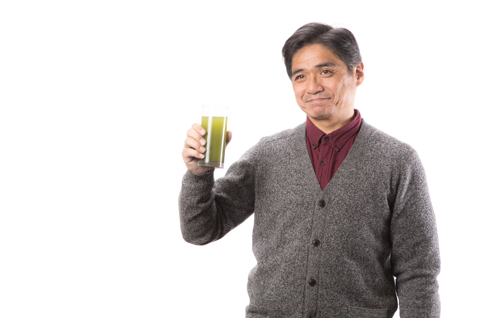 グレーのカーディガンを着た中年男性が青汁の入ったグラスを持って笑顔を見せている［モデル：よたか］