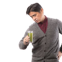 グラスの青汁を疑いながら覗き込む中年男性の写真