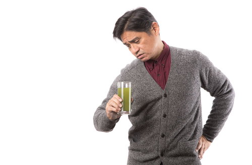 グラスの青汁を疑いながら覗き込む中年男性