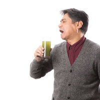 苦くて濃い青汁を飲んで渋い顔をする中年男性の写真