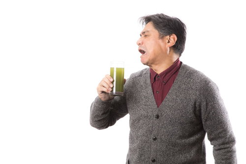 苦くて濃い青汁を飲んで渋い顔をする中年男性
