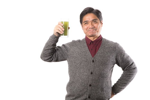 私の元気の秘密はこの青汁です！グラスを持つ健康的な中年男性