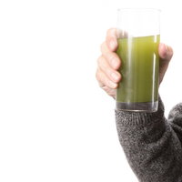 青汁のグラスを持つ右手とグレーセーター、健康飲料の写真