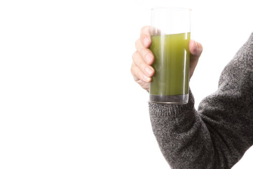 青汁のグラスを持つ右手とグレーセーター、健康飲料