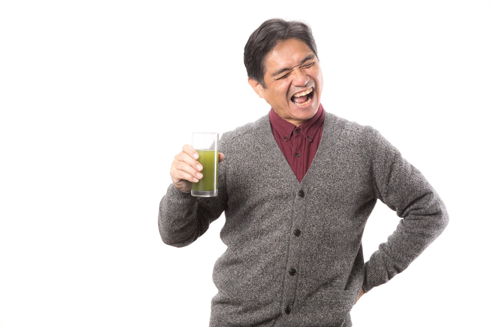 青汁を飲んで苦い表情をしながらも笑顔を見せる中年男性［モデル：よたか］