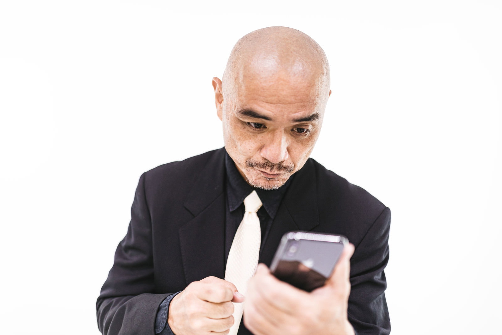 黒いスーツを着た坊主頭の中年男性がスマートフォンの画面を見つめ驚いている［モデル：よたか］