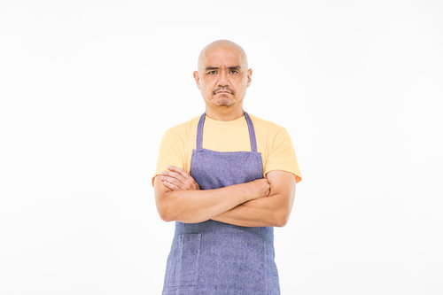 納得がいかない坊主頭の店主 青いエプロンを着た中年男性