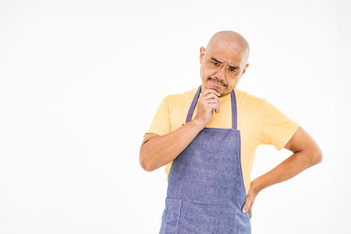 青いエプロンを着て考え込むスキンヘッドの中年男性