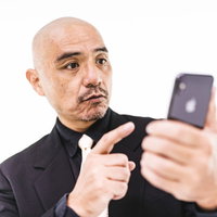 本日のスケジュールをスマホでチェックするスキンヘッドの中年男性の写真