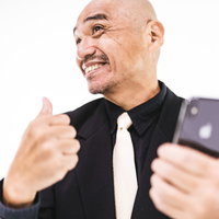 リセマラ成功でスマホを見て親指を立てる坊主の中年男性の写真