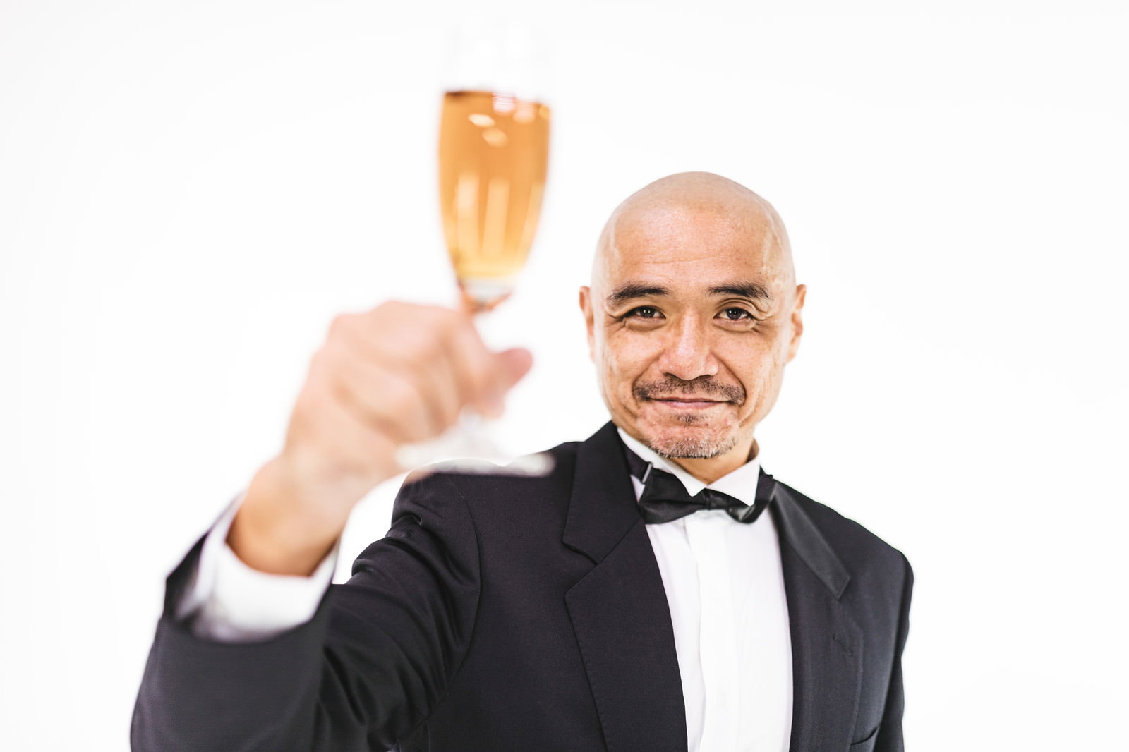 シャンパングラスを掲げて乾杯する黒いタキシード姿の男性［モデル：よたか］